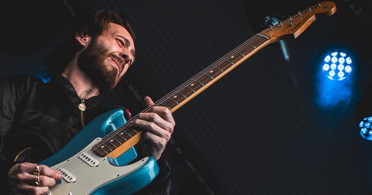Gitarist The Hague Blues speelt vol passie een solo op blauw met witte gitaar. Gitarist The Hague Blues speelt vol passie een solo op blauw met witte gitaar.