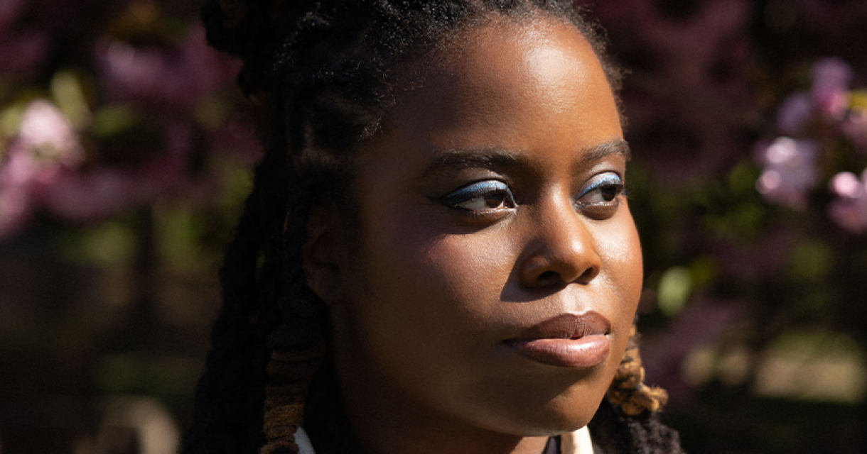 Portret van Yasmin Williams met blauwe oogschaduw en bloesem bomen op de achtergrond. Portret van Yasmin Williams met blauwe oogschaduw en bloesem bomen op de achtergrond.