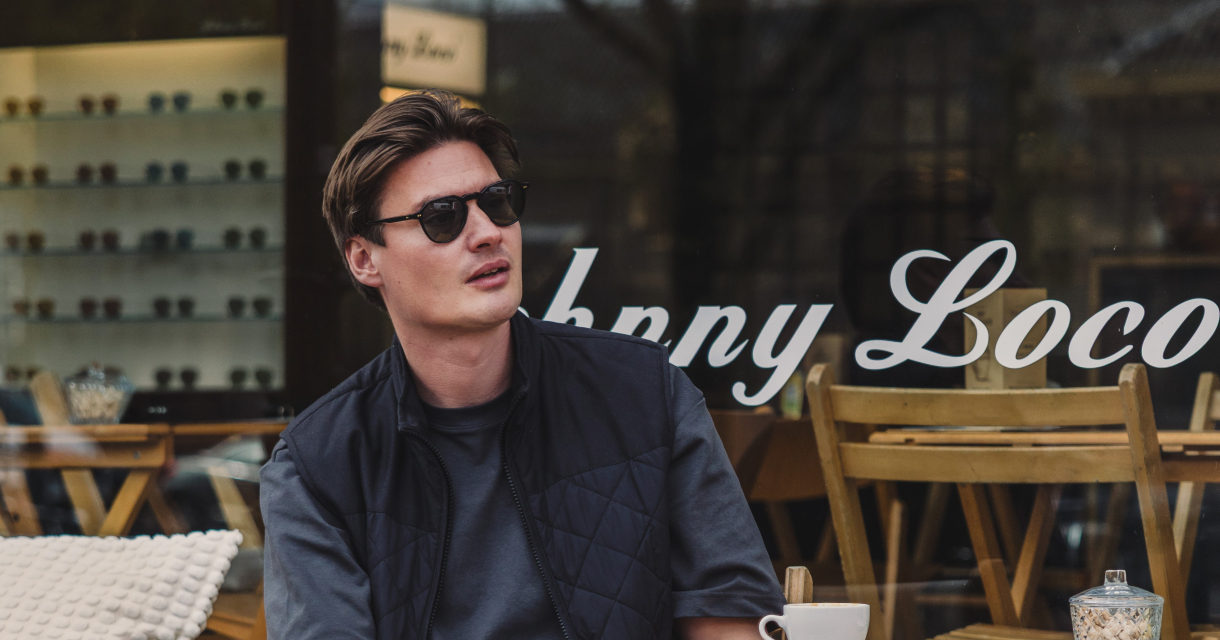 Jonge man zit relaxed met koffie op een terras voor Johnny Loco in Den Haag, gekleed in een casual outfit met zonnebril. Jonge man zit relaxed met koffie op een terras voor Johnny Loco in Den Haag, gekleed in een casual outfit met zonnebril.