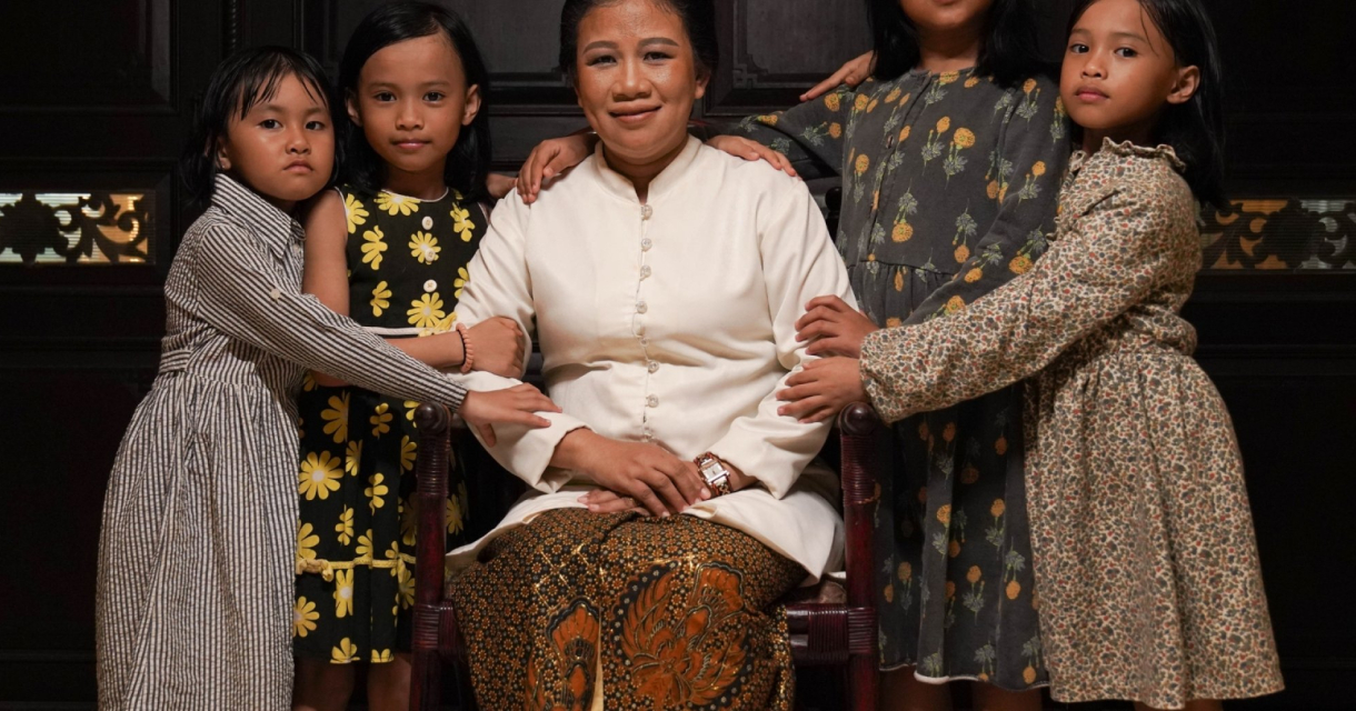 Een vrouw in traditionele kleding zit omringd door vijf jonge meisjes in jurken, die haar liefdevol vasthouden. Een vrouw in traditionele kleding zit omringd door vijf jonge meisjes in jurken, die haar liefdevol vasthouden.