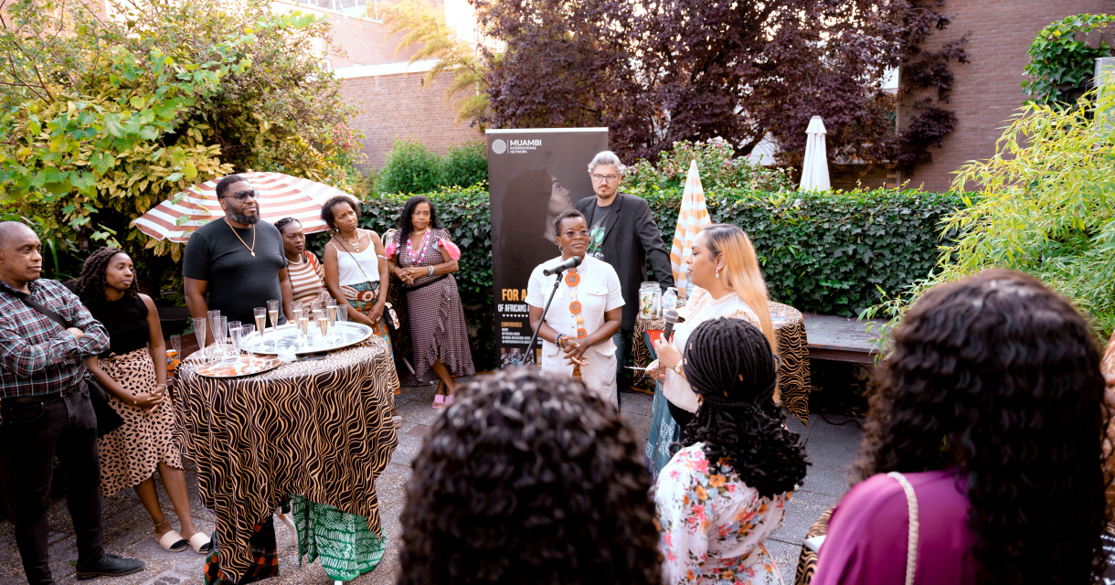 Bijeenkomst in een groene binnentuin met sprekers en genodigden tijdens een cultureel evenement van Miambi Foundation. Bijeenkomst in een groene binnentuin met sprekers en genodigden tijdens een cultureel evenement van Miambi Foundation.