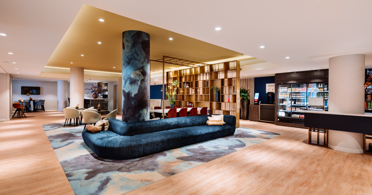 De moderne lobby van het Novotel World Forum met luxe zithoeken, warme verlichting en een stijlvolle bar met drankencollectie. De moderne lobby van het Novotel World Forum met luxe zithoeken, warme verlichting en een stijlvolle bar met drankencollectie.