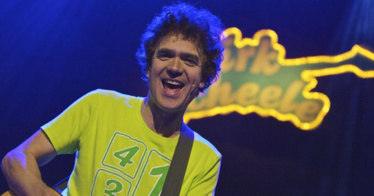 Dirk Scheele vrolijk en spelend op gitaar op podium in geel shirt en geel bandlogo met zijn naam erin passend bij zijn kindervoorstelling popconcert Foto: Guido Breedveld Dirk Scheele vrolijk en spelend op gitaar op podium in geel shirt en geel bandlogo met zijn naam erin passend bij zijn kindervoorstelling popconcert Foto: Guido Breedveld