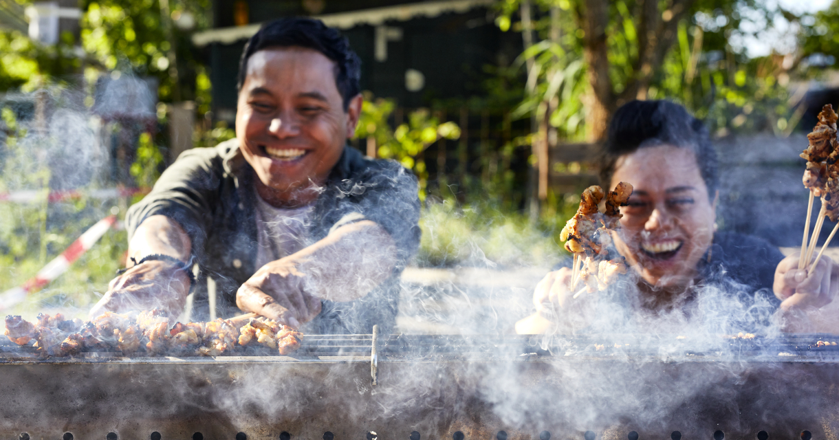 Twee mensen grillen lachend saté op barbecue Twee mensen grillen lachend saté op barbecue