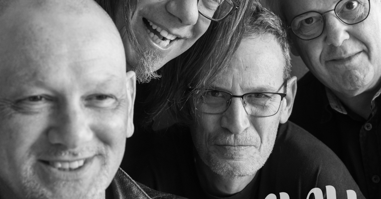 Zwart wit bandfoto van Slau enthousiast en lachend ingezoomd in de camera. Zwart wit bandfoto van Slau enthousiast en lachend ingezoomd in de camera.