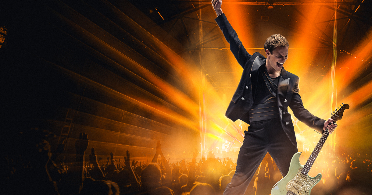 Rockzanger met gitaar voor juichend publiek op podium (c) We Will Rock You 