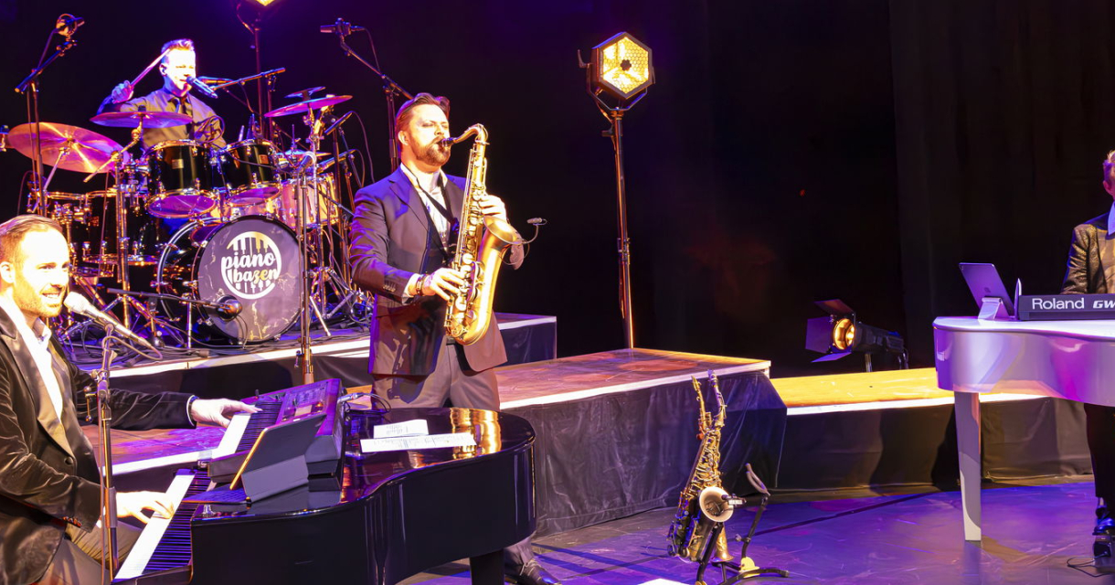 De leden van de Pianobazen staan op het podium met hun instrumenten. De leden van de Pianobazen staan op het podium met hun instrumenten.