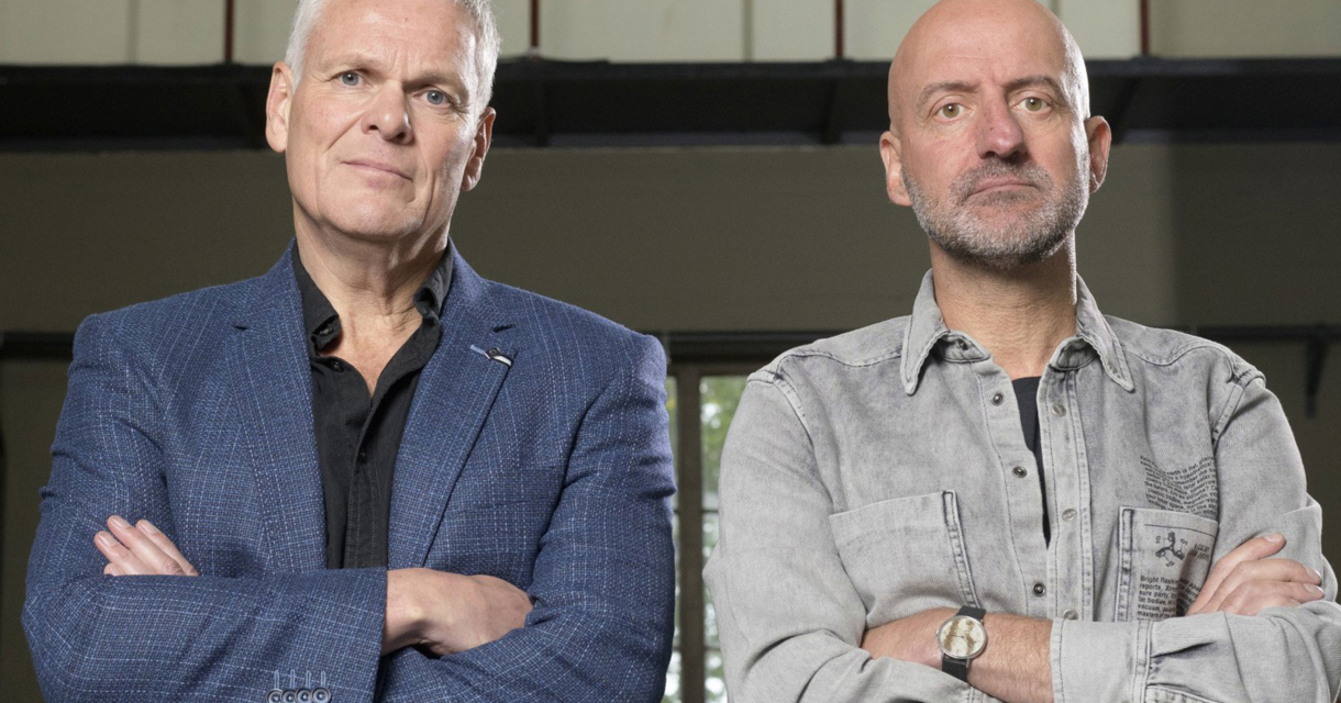 Joep van Deudekom en Rob Urgert poseren naast elkaar met een serieuze blik en hun armen over elkaar. Joep van Deudekom en Rob Urgert poseren naast elkaar met een serieuze blik en hun armen over elkaar.
