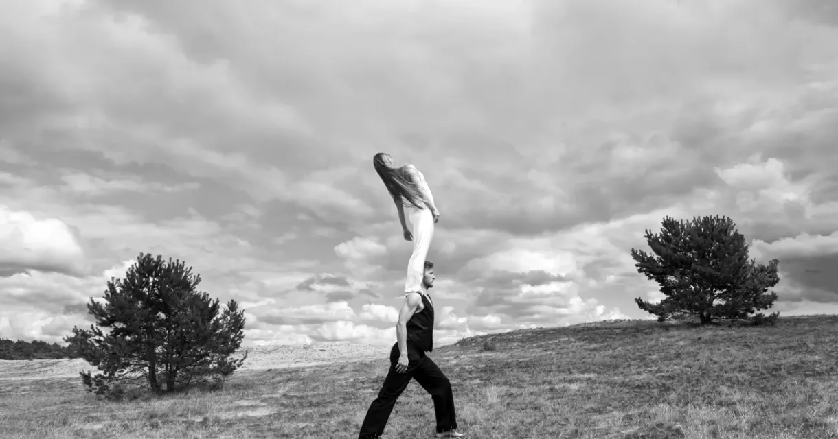 Twee mensen doen een acrobatische lift op een open veld met bomen en een bewolkte lucht Twee mensen doen een acrobatische lift op een open veld met bomen en een bewolkte lucht
