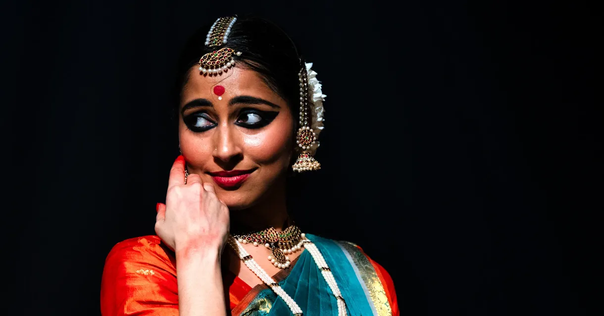 Klassieke danseres in kleurrijke sari en sieraden poseert tegen donkere achtergrond met expressieve blik Klassieke danseres in kleurrijke sari en sieraden poseert tegen donkere achtergrond met expressieve blik