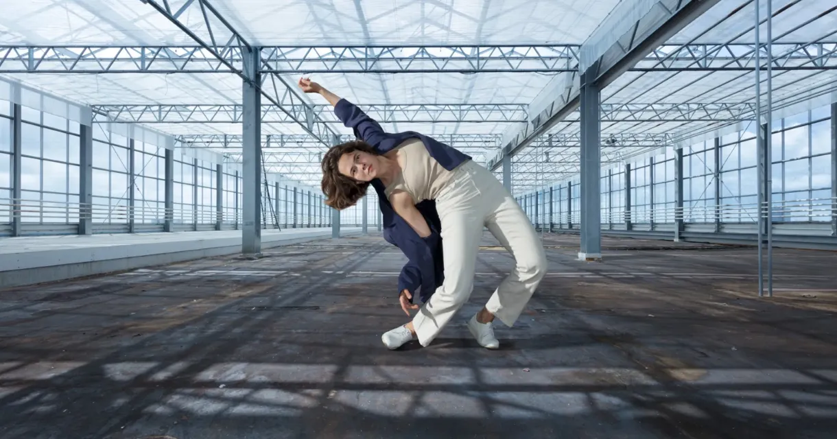 danser in een moderne pose in een lege, glazen kas met stalen constructie danser in een moderne pose in een lege, glazen kas met stalen constructie