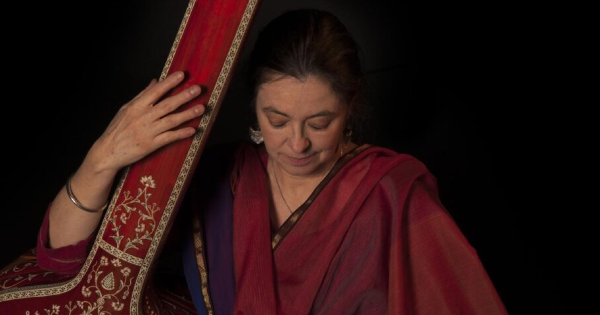 Portret van Dhrupad Marianne Svasek met Indiase snaarinstrument en in traditionele rode kleding.