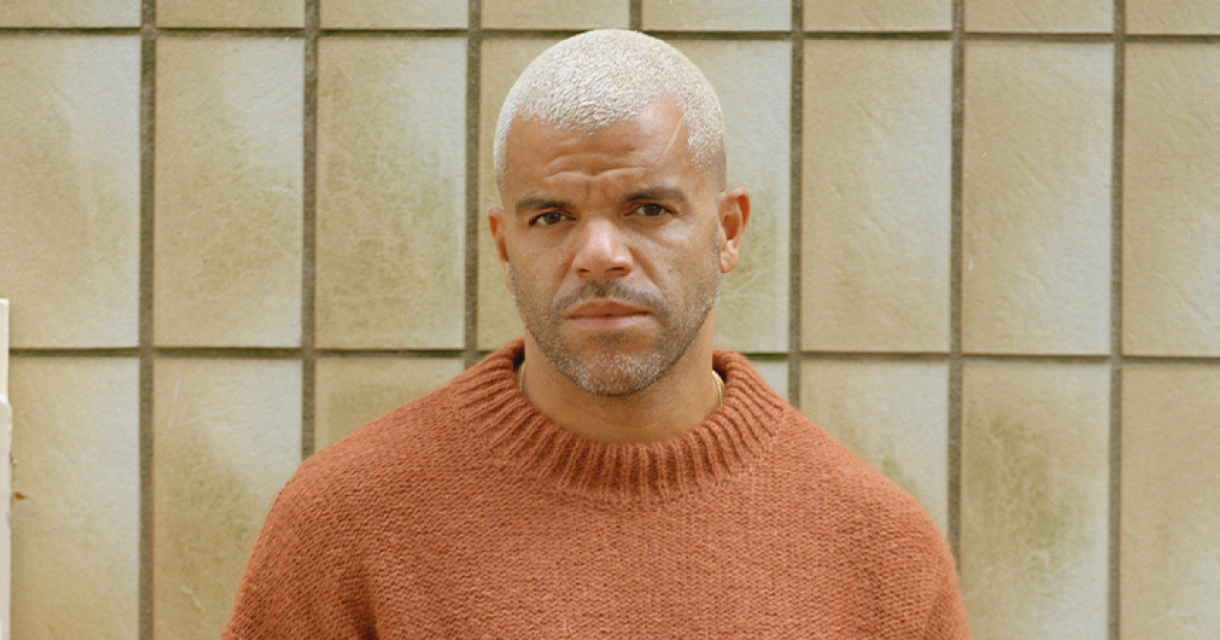 Zanger Sef serieus kijkend met een tegel achtergrond.