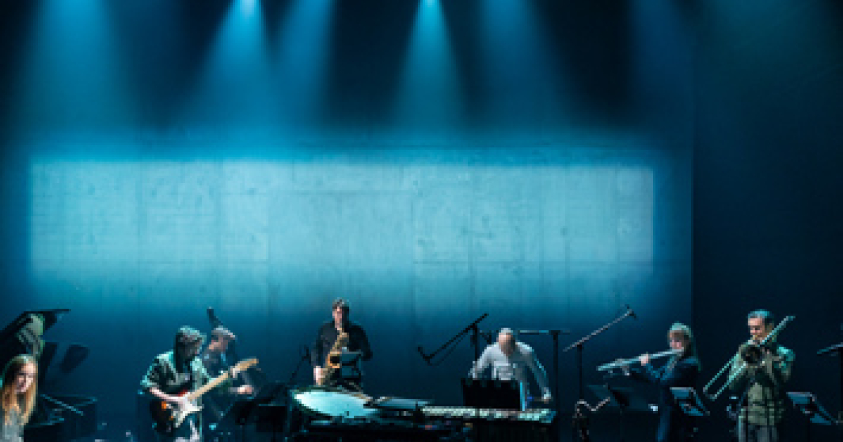 Het muziek ensemble Klang staat met hun instrumenten op een blauw verlicht podium Het muziek ensemble Klang staat met hun instrumenten op een blauw verlicht podium