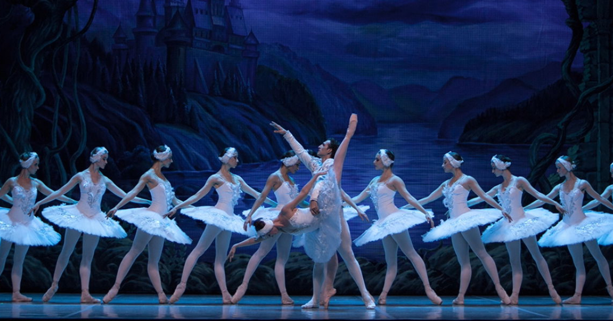 Balletdansers staan in hun witte tutu's en kostuums op het podium tijdens de productie van het zwanenmeer. 
