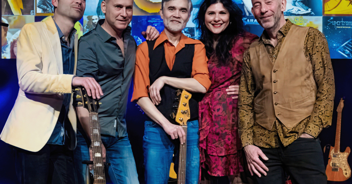 De leden van The 70's unplugged kijken lachend in de camera. Ze staan voor een achtergrond met sfeerfoto's uit de jaren 70.