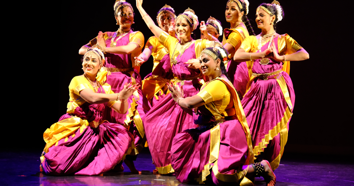 Groep dansers in kleurrijke Indiase kostuums poseert op een podium tijdens een klassieke dansvoorstelling