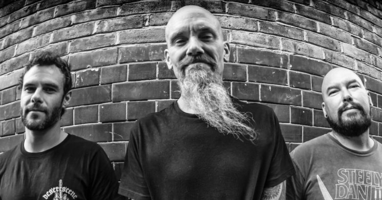 Zwart wit portret van Hardrock band Mondo Generator poserend tegen bakstenen muur.