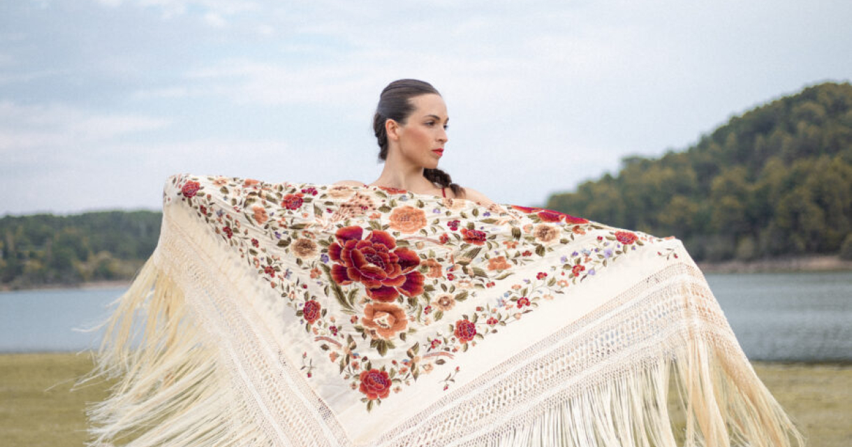 Foto in een Mediterrane omgeving met een meer en berg op de achtergrond waarin flamencodanseres Marina Paje met een mooie omslagdoek met opengestrekte armen staat.