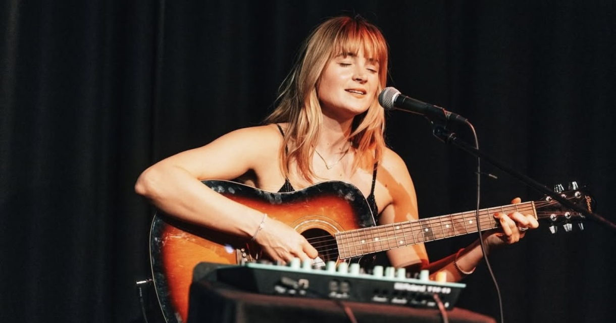 Een vrouwelijke artiest spelend op haar gitaar op het podium