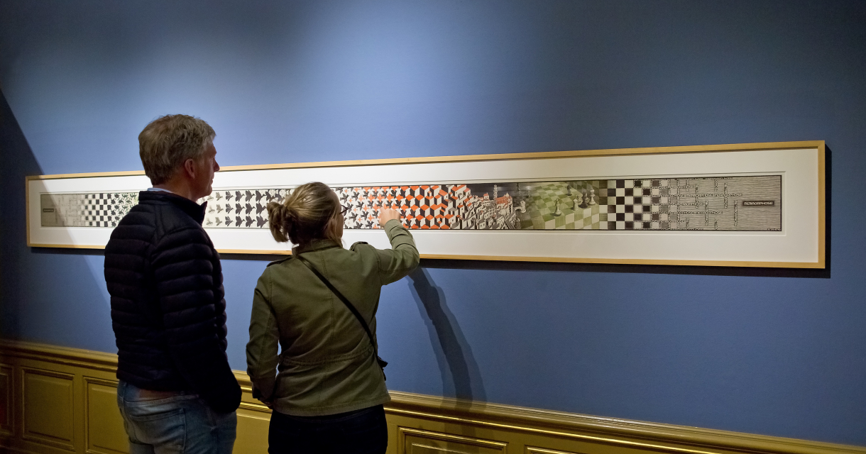 Man en vrouw kijken naar één van de kunstwerken van M.C. Escher