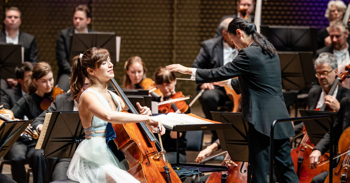 Dirigent leidt een orkest terwijl een celliste een solo speelt tijdens een concert. Dirigent leidt een orkest terwijl een celliste een solo speelt tijdens een concert.