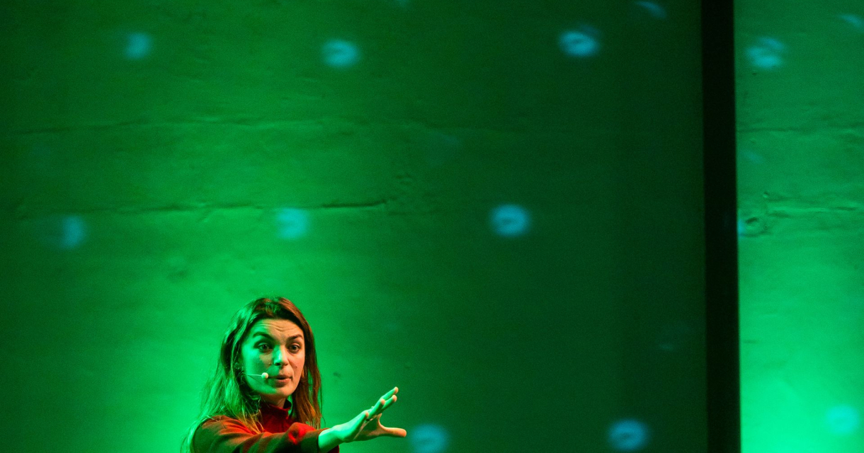 Vrouw op een groen verlichte podiumvloer tijdens een presentatie of theatervoorstelling. Vrouw op een groen verlichte podiumvloer tijdens een presentatie of theatervoorstelling.