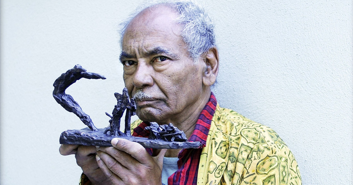 An elderly man holds a sculpture in his hands.