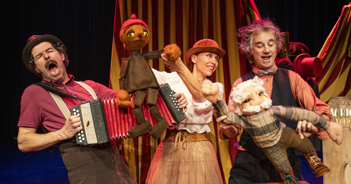 Drie performers tijdens een poppenkastvoorstelling met kleurrijke poppen.