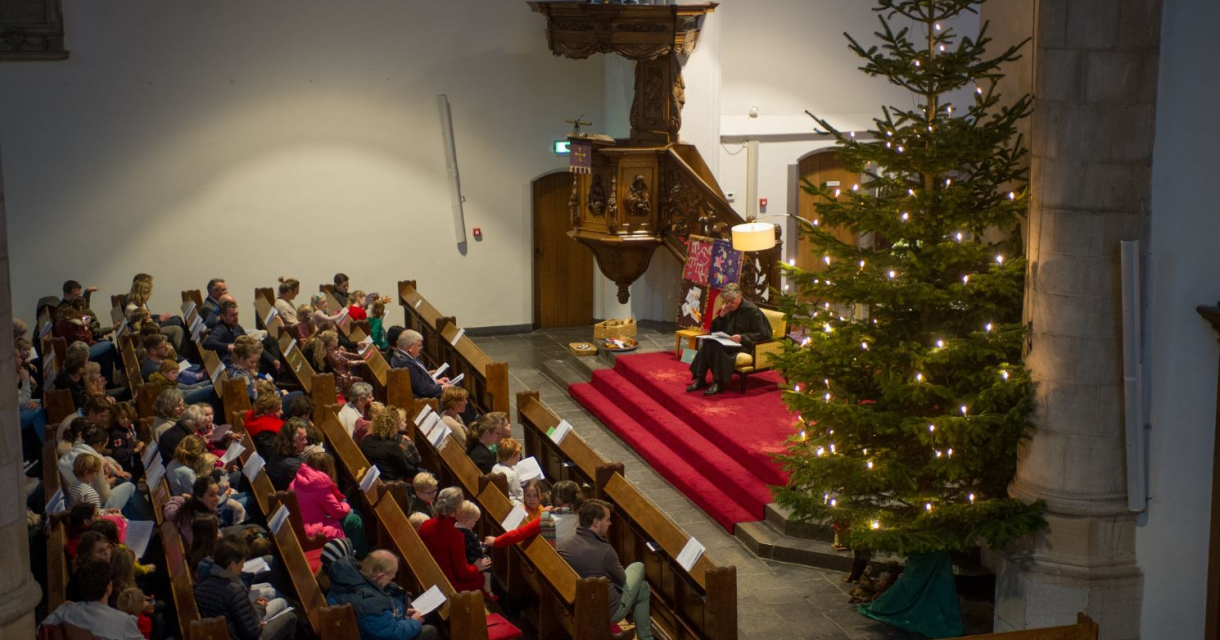 Een volle kerk tijdens een kerstbijeenkomst met een kerstboom.