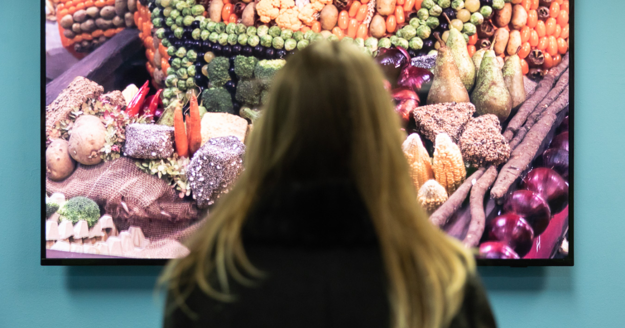 Een vrouw met lang haar kijkt naar een scherm met kleurrijke groenten.