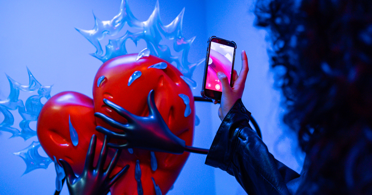 Rood hartsculptuur met handen en een smartphone.