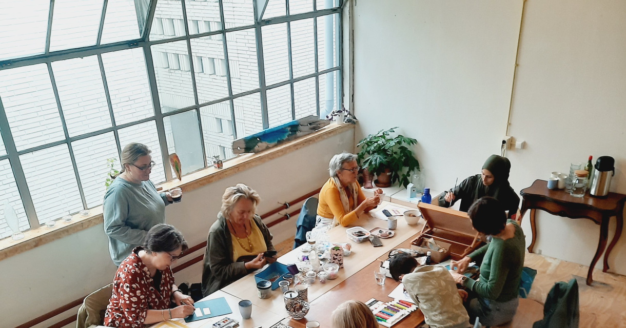 Een groep vrouwen aan een tafel die aan het tekenen en schilderen zijn. 