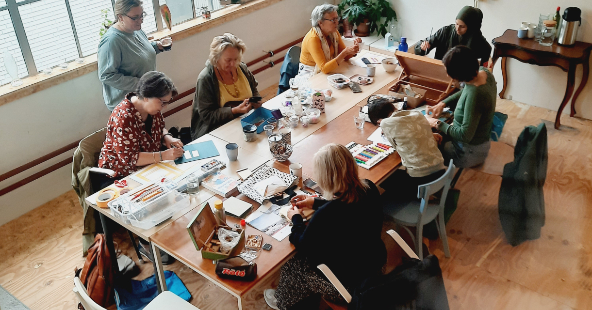 Een groep vrouwen aan een tafel die aan het tekenen en schilderen zijn. 