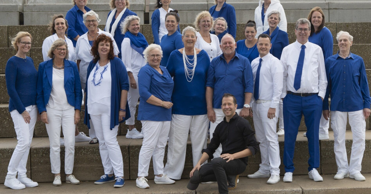 Een zanggroep van 20 mensen in blauwe en witte kleding.
