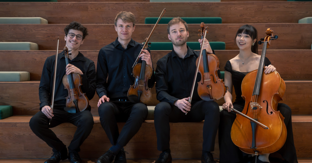Vier muzikanten in zwarte kleding met strijkinstrumenten zitten op een houten tribune.