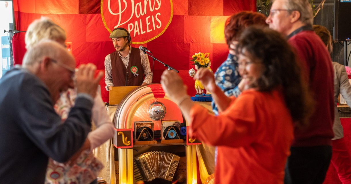 Mensen dansen vrolijk in het Danspaleis met kleurrijke achtergrond.