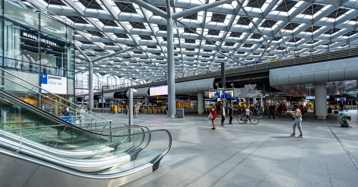 Ingang van een modern treinstation met mensen en roltrappen