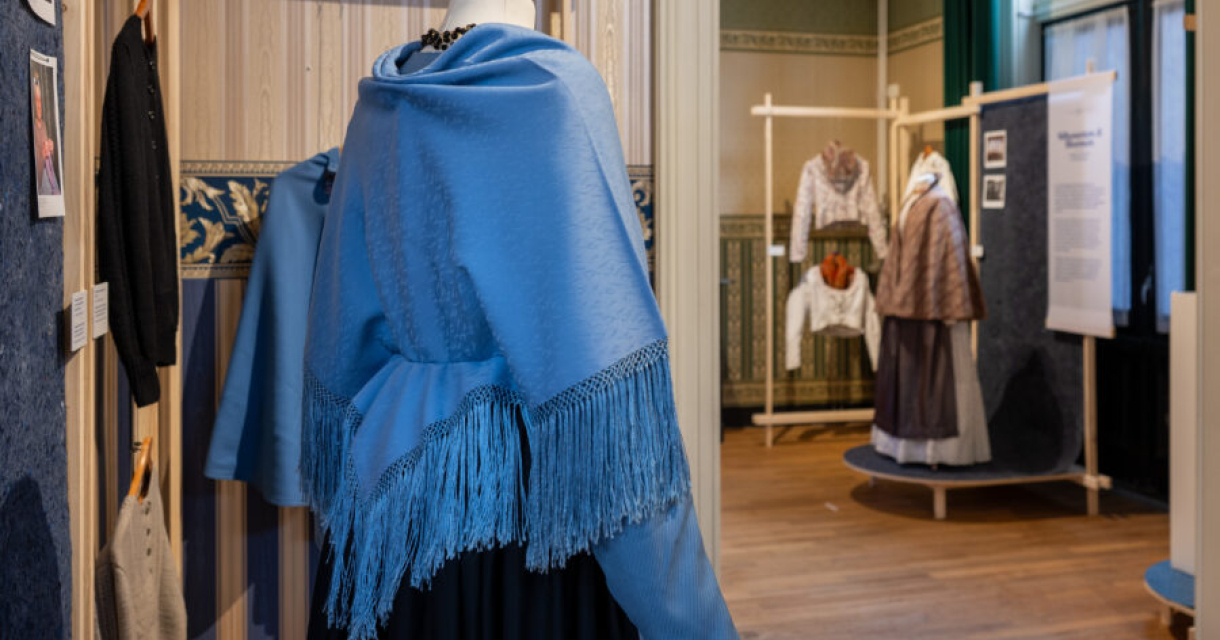 Een blauwe sjaal met franjes hangt naast andere kledingstukken.