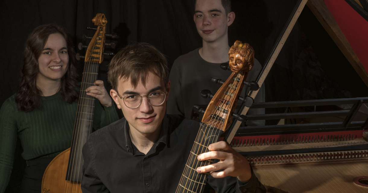 Drie jonge muzikanten poseren met een luit en een klavecimbel.
