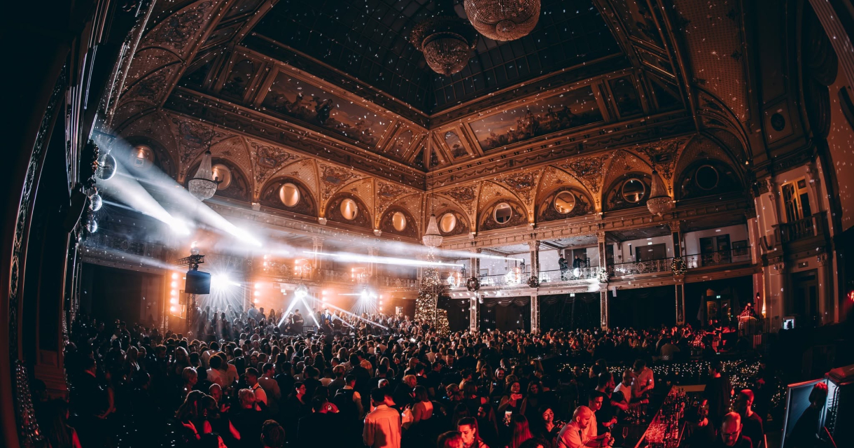 People dancing and celebrating in a festive hall with light shows.