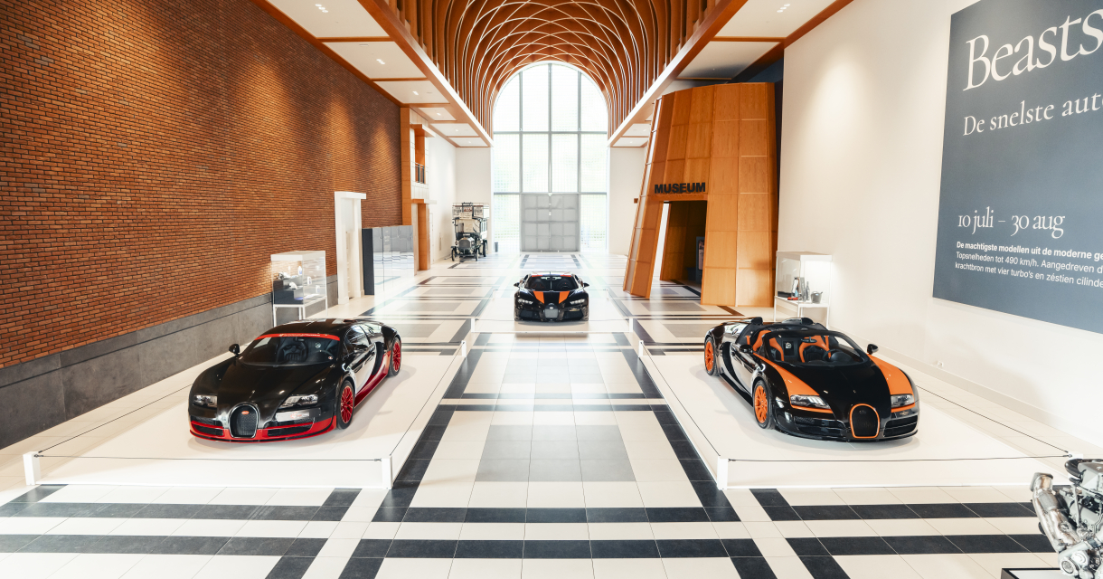 Three Bugatti sports cars are displayed in a museum hall.