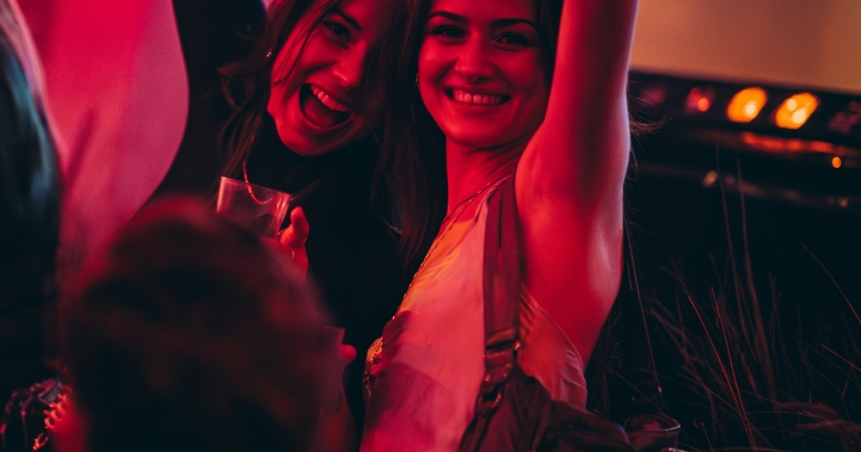 Two women smiling and raising their arms in a festive setting.