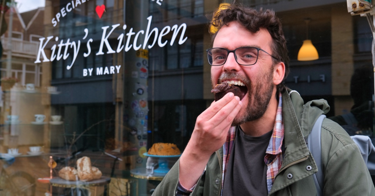 Een man eet een gebakje voor het raam van Kitty's Kitchen.