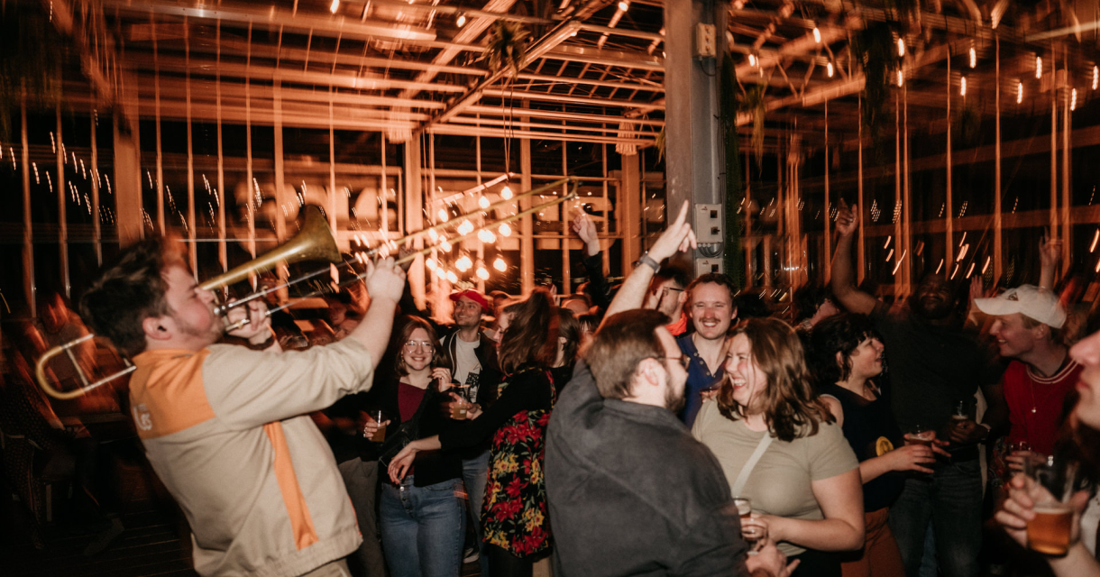 Een man speelt trombone terwijl mensen dansen en genieten. (c) Louise Boonstoppel
