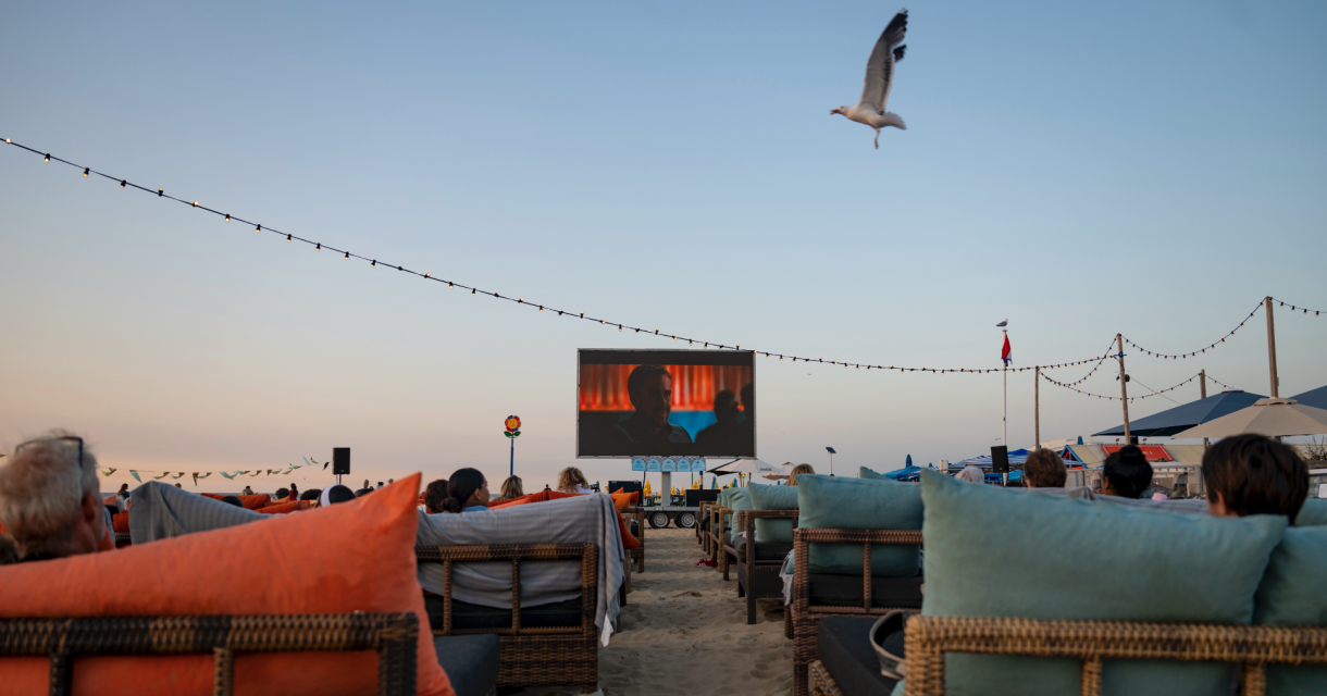 Mensen kijken naar een film op een groot scherm op het strand