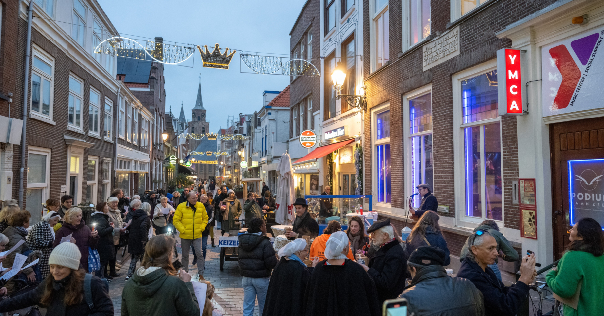 Mensen in een straat in Den Haag tijdens een evenement, met kerstverlichting en een muziekant