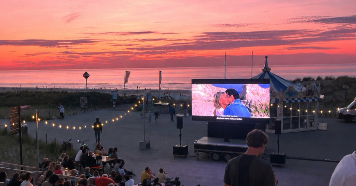 Mensen zitten op trappen als ze een film kijken bij zonsondergang op het strand.