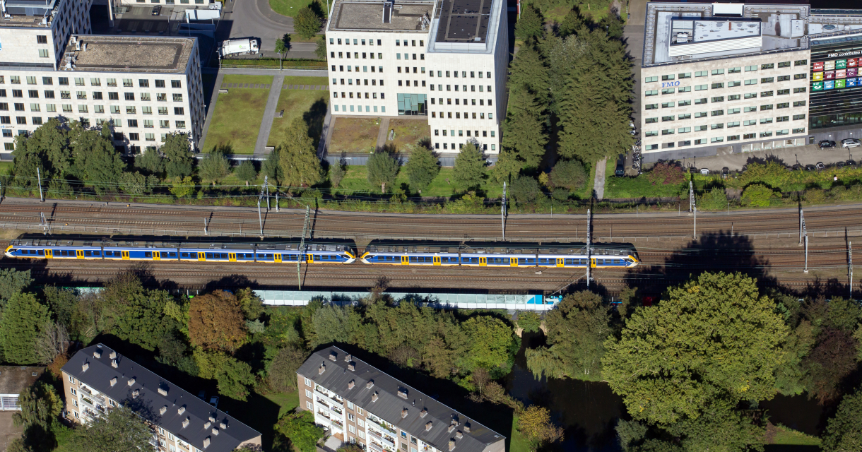 Een trein rijdt langs een groenperk en moderne gebouwen.