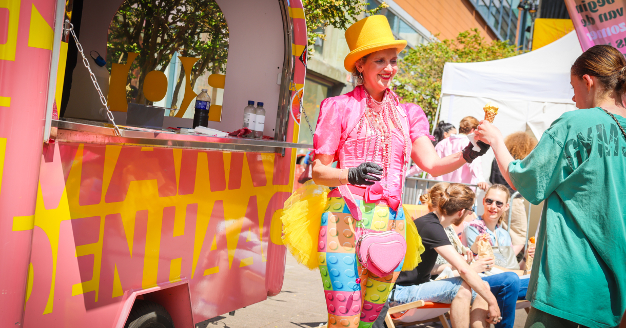 A woman in colorful clothing hands ice cream to a girl at an ice cream cart.